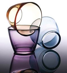 three different colored glass vases sitting next to each other on a reflective table top