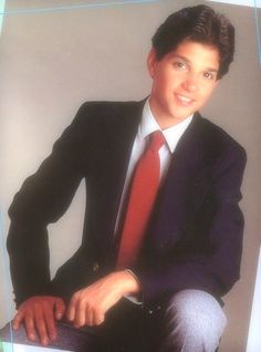 a young man in a suit and tie posing for a photo with his hands on his knees