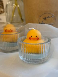 two small yellow rubber ducks sitting in glass dishes on a white tablecloth covered table