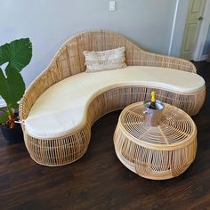 a wicker couch and ottoman in a room with wood flooring next to a potted plant