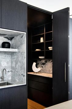 a kitchen with marble counter tops and black cabinet doors open to reveal a white sink