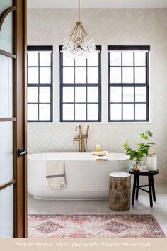 a white bath tub sitting next to a window in a bathroom under a chandelier