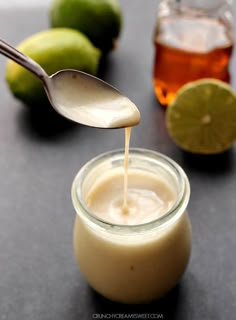 a spoon pouring honey into a jar filled with lemons and limes on a table