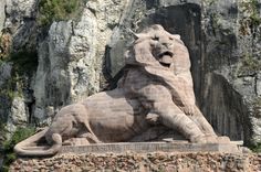 a stone lion statue sitting in front of a rocky cliff face with its mouth open