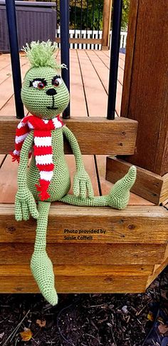 a green stuffed animal sitting on top of a wooden bench with a red and white scarf around it's neck