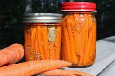 carrots and other vegetables are in jars on a wooden table outside with trees in the background