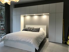 a white bed sitting in a bedroom next to a wall mounted light above it's headboard