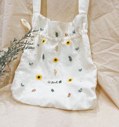 a white bag with sunflowers on it sitting next to a plant and some fabric