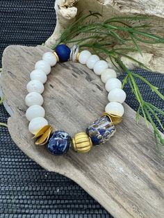 Enhance your accessory collection with this exquisite artisanal bracelet by JP Designs. Featuring natural bone beads, a striking blue druzy agate bead, a vibrant lampwork bead, and a unique ceramic bead, this bracelet is a perfect blend of rustic charm and elegant sophistication. Accentuated with gold-tone elements, this piece is versatile and ideal for any occasion, whether casual or formal. Materials: Natural Bone Beads: The smooth, ivory-colored bone beads offer a rustic yet refined look, providing a neutral base that complements any outfit. Blue Druzy Agate: Known for its sparkling surface and vibrant blue color, blue druzy agate is believed to promote relaxation and stress relief while adding a unique, eye-catching texture to the bracelet. Lampwork Bead: Handcrafted with vibrant color Artisan Hand-strung White Bracelets, Artisan White Hand-strung Bracelets, Artisan Hand-strung White Bracelet, Artisan White Bracelets With Large Beads, Artisan White Bracelet With Large Beads, Unique White Bracelets With Large Beads, Unique White Bracelet With Large Beads, White Artisan Beaded Bracelets, Artisan White Beaded Bracelets