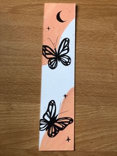 a bookmark with two butterflies on it sitting on a table next to a clock