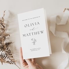 a person holding up a wedding book next to a plant