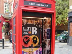 a red phone booth on the side of the street with posters and earbuds