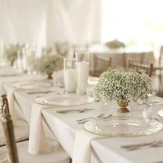 the table is set with white linens and baby's breath centerpieces