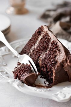 a slice of chocolate cake on a white plate with a fork in it and another piece missing