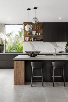 a modern kitchen with black cabinets and marble counter tops, two bar stools at the island