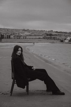 a black and white photo of a woman sitting in a chair on the beach with her legs crossed