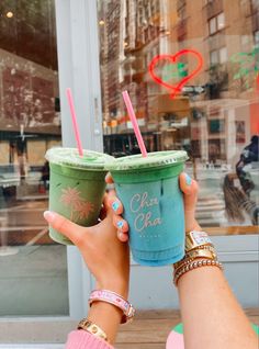 two people holding up cups in front of a window