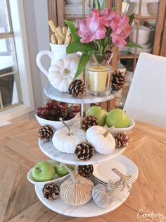 a three tiered tray with apples, pears and pine cones on the top