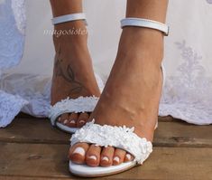 a woman's feet wearing white sandals with flowers on them and lace around the toes