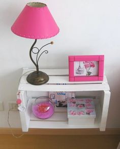 a pink lamp sitting on top of a white table next to a shelf with pictures