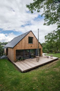 a wooden deck in front of a house with a black roof and two chairs on it