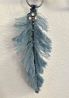 a blue feather keychain hanging from a hook on a white wall with beads