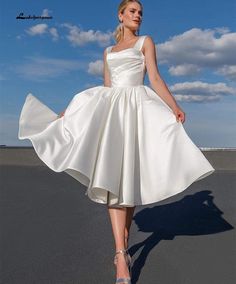 a woman in a white dress is standing on the pavement with her hands behind her back