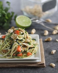 a white plate topped with pasta covered in veggies next to a lime wedge