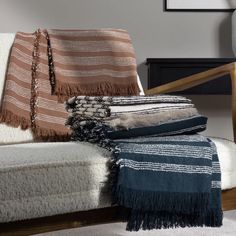 several blankets and pillows on a couch in a room with a wooden arm chair, white carpet and black framed artwork