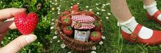 someone is holding a strawberry in their hand next to a basket of strawberries and a bottle of jam