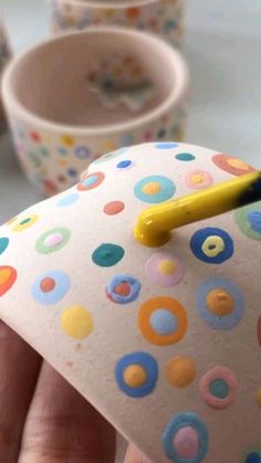 a hand holding a yellow toothbrush in it's right hand next to some cups