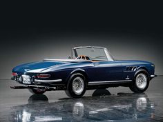 an old blue sports car is parked in a dark room with its hood up and the top down