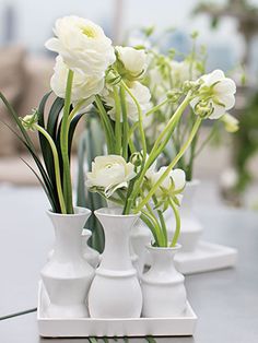 four white vases with flowers in them on a table