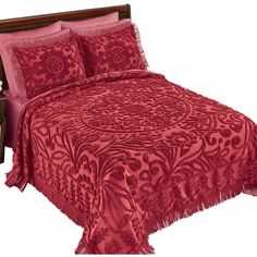 a bed with red bedspread and pillows on top of it, next to a night stand