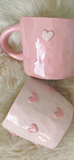 two pink mugs sitting on top of a white fur covered floor next to each other