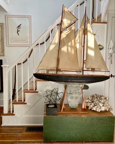 a model sailboat sitting on top of a wooden box in front of a stair case