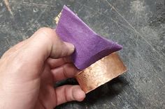 a hand holding a piece of purple cloth in it's left hand with a gold band