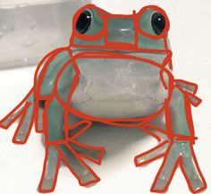 a green frog with red lines on it's body and eyes, sitting on a white surface