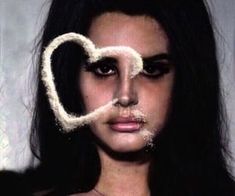 a woman with long black hair and white make - up holding a heart shaped object in front of her face