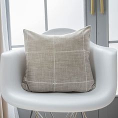 a white chair with a pillow on top of it next to a window in a room