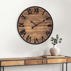 a large wooden clock mounted to the side of a wall next to a table with a vase on it