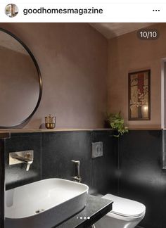 a white toilet sitting next to a bathroom sink under a round mirror on a wall