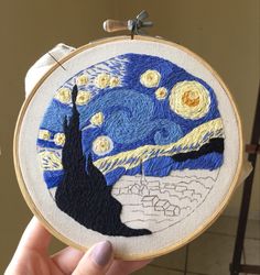 someone is holding up a hand embroidered art piece that looks like the starry night