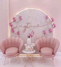 pink chairs and a table in front of a white wall with flowers on the top