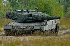 an army tank with camouflage on it driving through the grass and trees in the background