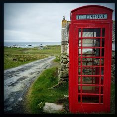 a red telephone booth sitting on the side of a road next to a stone wall