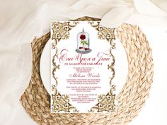 a white and gold wedding card with a red rose on the top is sitting in a wicker basket