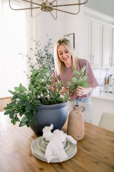 a woman standing in front of a potted plant on top of a wooden table