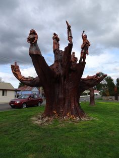 a large tree with people carved into it's trunk in the grass next to a red car