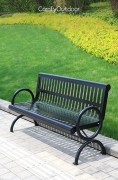 a black park bench sitting on top of a brick walkway next to a lush green field